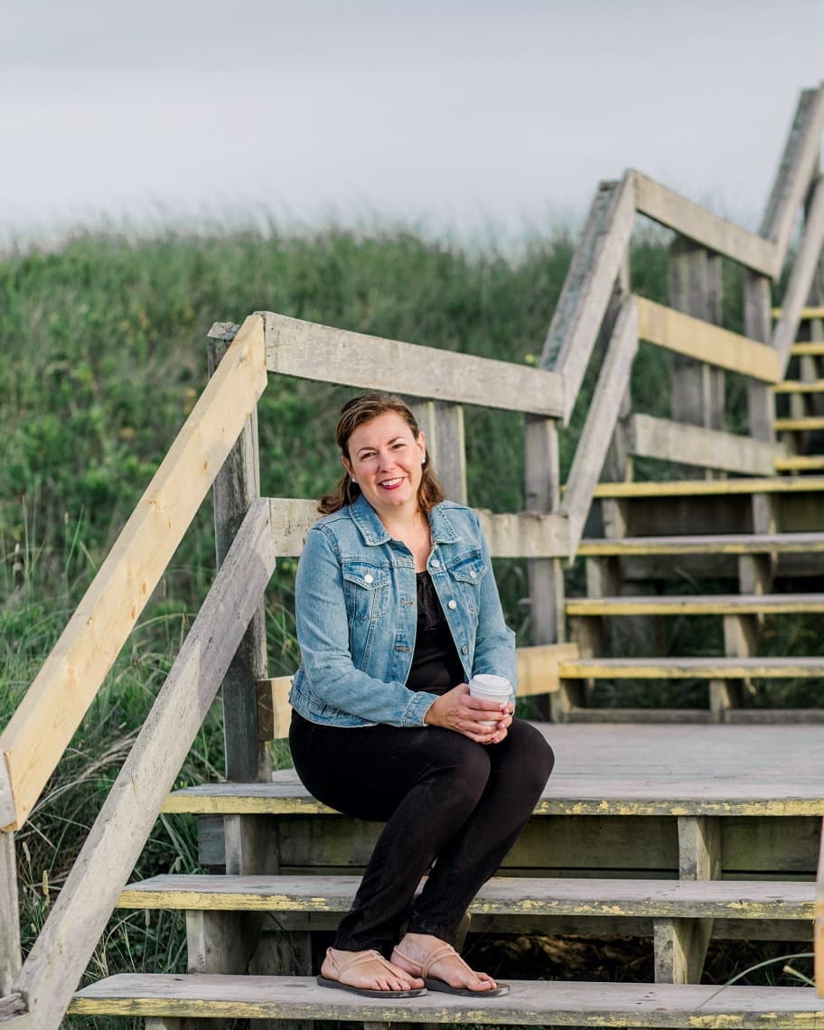 Andrea Van Hal sits on a set of steps, leading to a beach.